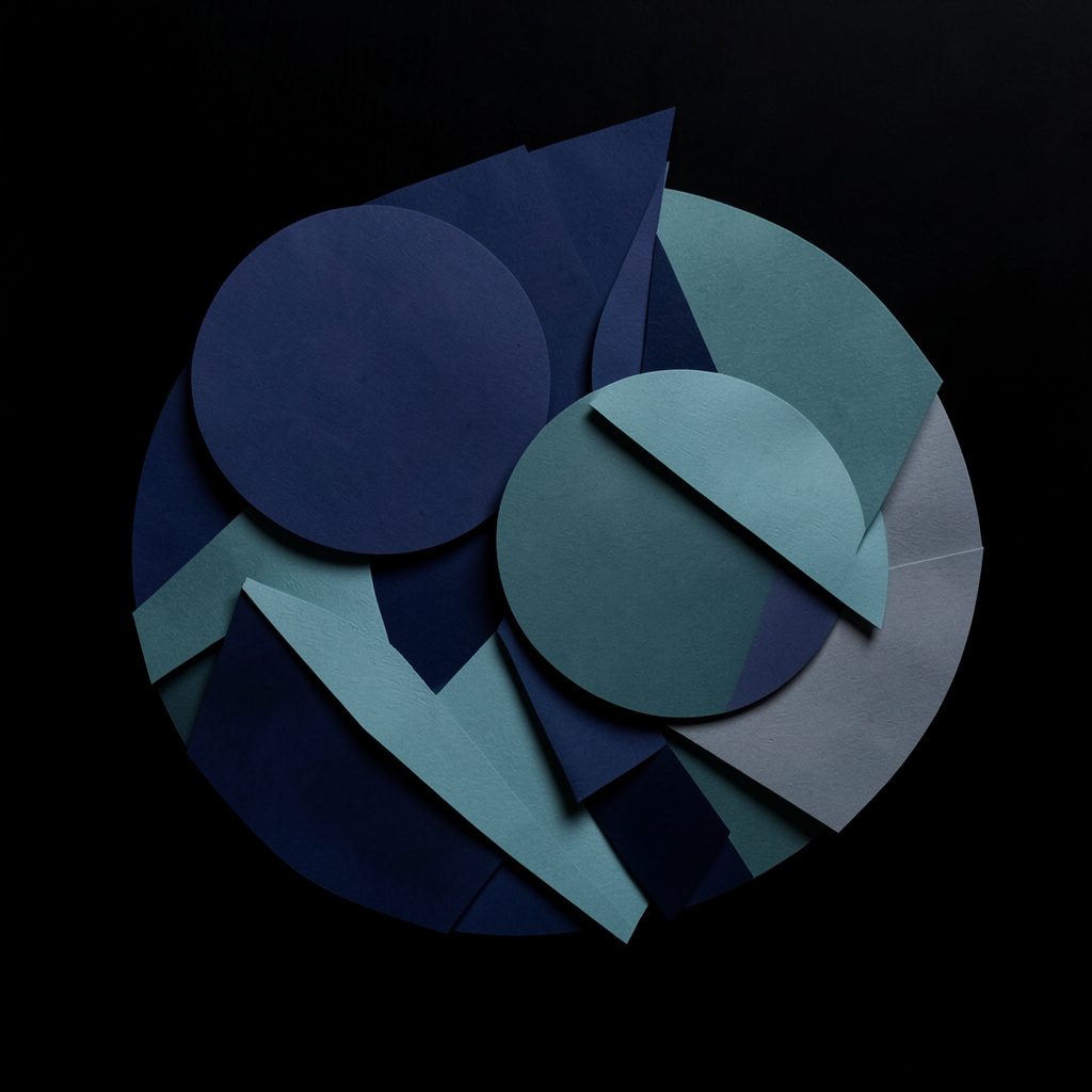A layered paper cut-out collage of overlapping geometric circles and soft angular shards in deep navy, muted teal, and slate grey, forming an abstract emblem against a near-black background